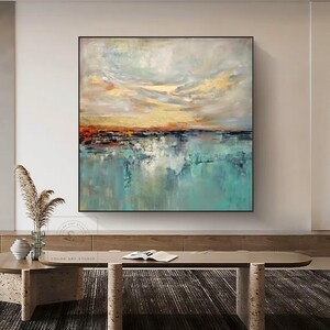 May include: Abstract landscape painting with a square black frame. The artwork features a vibrant color palette of teal, gold, orange, and gray, depicting a serene waterscape under a dynamic sky. The painting is signed "COLOR ART STUDIO".