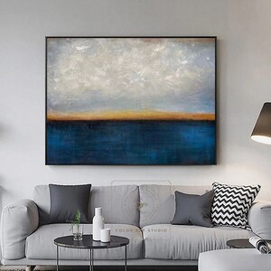 Puede incluir: Pintura abstracta de un paisaje mar&iacute;timo con un oc&eacute;ano azul, un horizonte naranja delgado y nubes blancas sobre un cielo gris claro. La pintura est&aacute; enmarcada en negro.