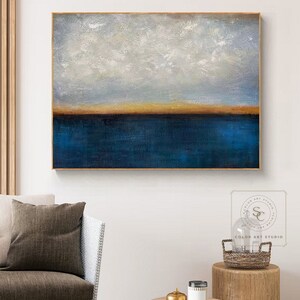 Puede incluir: Pintura abstracta con una combinaci&oacute;n de colores azul y dorado. La pintura representa un horizonte con un cielo azul y nubes blancas sobre un cuerpo de agua azul con una fina l&iacute;nea dorada que separa el cielo y el agua.