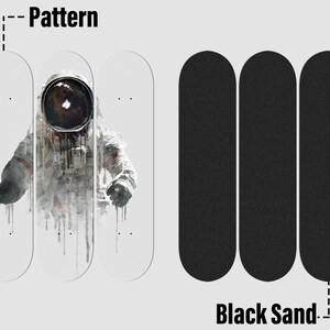 May include: Three blank skateboard decks with a graphic of an astronaut in a white spacesuit with a black helmet. The astronaut is in front of a white background with black and gray paint splatters. The decks are arranged in a row with the astronaut in the middle. The decks are labeled "Pattern". Three black skateboard grip tape sheets are arranged in a row below the decks. The grip tape sheets are labeled "Black Sand".