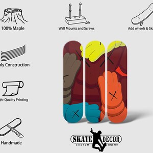 Op de afbeelding: Drie skateboard decks met een kleurrijk grafisch ontwerp met een cartoonfiguur in rood, geel, blauw en oranje. De decks zijn gemaakt van 7-laags esdoornhout en zijn handgemaakt. De tekst "SKATE DECOR CUSTOM WALL ART" is onderaan de afbeelding gedrukt.