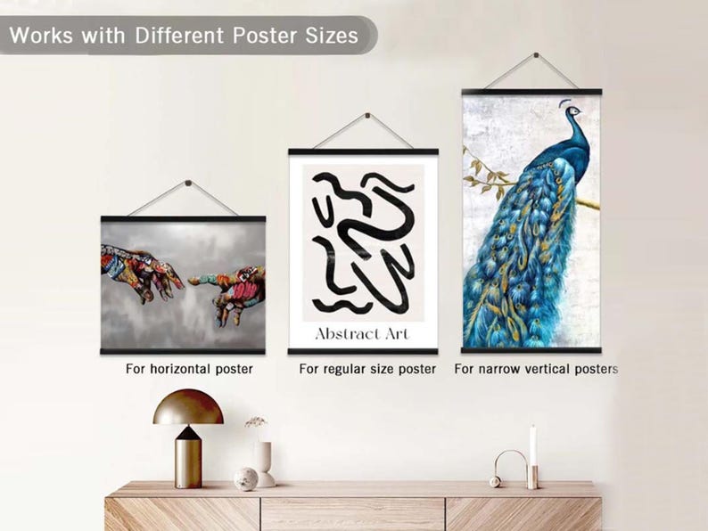 Pu&ograve; includere: Tre poster di diverse dimensioni appesi a una parete bianca utilizzando un sistema di sospensione con binari neri. I poster presentano un dipinto astratto colorato, un dipinto astratto in bianco e nero con il testo "Abstract Art" e un dipinto di un pavone con piume blu e verdi.