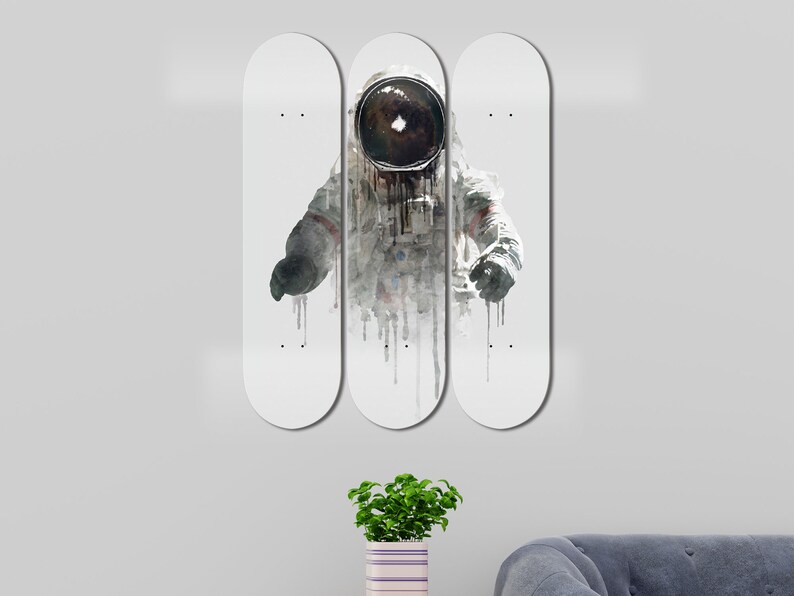 May include: Three white skateboard decks with a watercolor illustration of an astronaut in a spacesuit. The astronaut is wearing a helmet with a black visor. The illustration is in shades of gray and white.