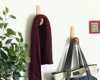 May include: Two wooden wall hooks with a unique curved design. One hook has a burgundy scarf hanging from it, while the other has a brown and white tote bag hanging from it.