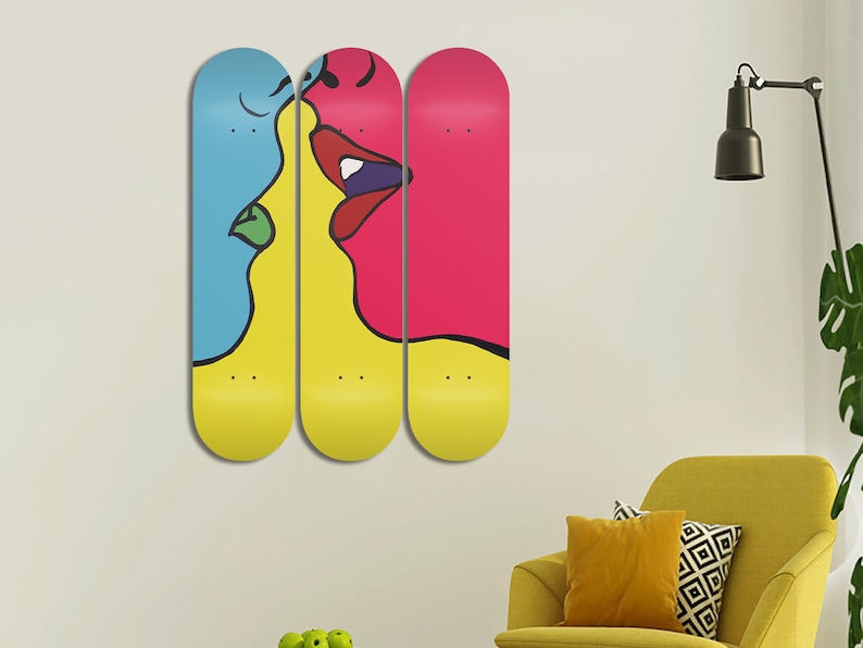 May include: Three skateboard decks with a colorful abstract painting of two faces kissing. The left face is blue, the middle face is yellow, and the right face is pink.