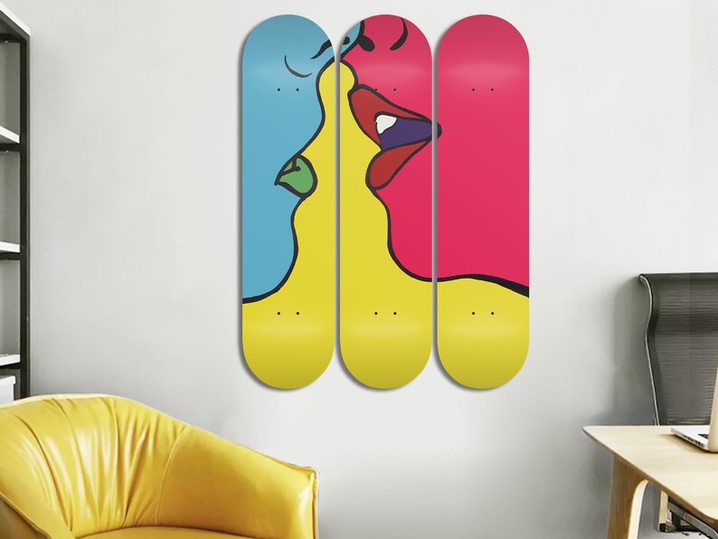 May include: Three yellow, blue, and pink skateboard decks with a black line drawing of two faces kissing. The faces are partially on each deck.
