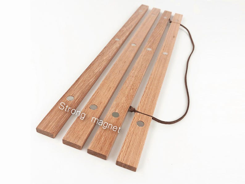 Puede incluir: Cuatro tiras de madera con un cord&oacute;n de cuero marr&oacute;n atado. Cada tira tiene un im&aacute;n plateado incrustado en la madera. El texto "Strong magnet" est&aacute; escrito en la madera.