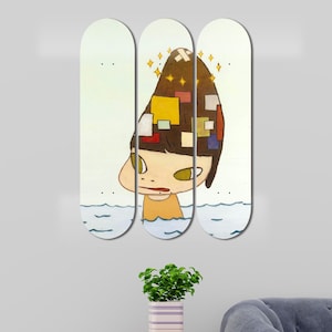 May include: Three skateboard decks featuring a colourful illustration of a girl with a head full of colourful blocks. The girl is wearing a brown shirt and is surrounded by blue water.