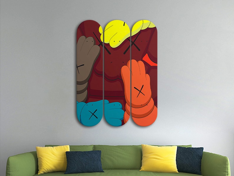 Op de afbeelding: Drie skateboard decks met een kleurrijk cartoonontwerp met een rode achtergrond, blauwe, gele, oranje en bruine handen en zwarte X'en.