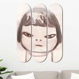 Op de afbeelding: Drie skateboard decks met een schilderij van een meisjesgezicht. Het meisje heeft bruin haar en kijkt recht naar de kijker. De achtergrond is lichtbeige.