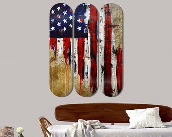 May include: Three wooden skateboard decks painted with an abstract American flag design. The flag is painted in red, white, and blue with drips of paint running down the decks. The decks are arranged horizontally.