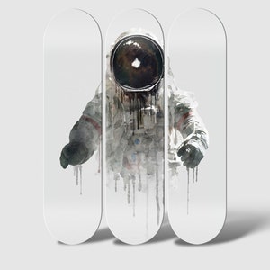 May include: Three white skateboard decks with a watercolor illustration of an astronaut in a spacesuit. The astronaut's helmet is black and the suit is white with black accents. The astronaut is depicted in a floating position with their arms outstretched.