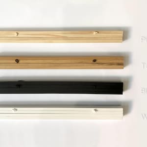 Puede incluir: Cuatro muestras de marcos de madera y pintados en cuatro acabados diferentes. El marco superior es de madera clara, etiquetado como "Pino". El segundo marco es de madera m&aacute;s oscura, etiquetado como "Teca". El tercer marco es negro, etiquetado como "Negro". El marco inferior es blanco, etiquetado como "Blanco".