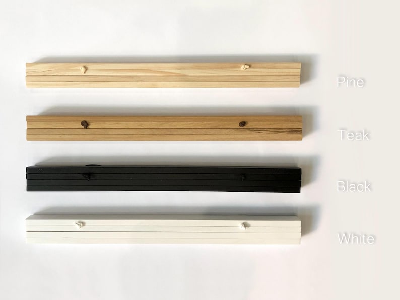 Puede incluir: Cuatro muestras de marcos de madera y pintados en cuatro acabados diferentes. El marco superior es de madera clara, etiquetado como "Pino". El segundo marco es de madera m&aacute;s oscura, etiquetado como "Teca". El tercer marco es negro, etiquetado como "Negro". El marco inferior es blanco, etiquetado como "Blanco".