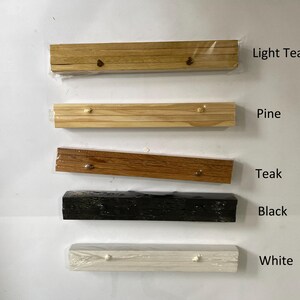 Pu&ograve; includere: Cinque cornici in legno di diversi colori: teak chiaro, pino, teak, nero e bianco. Le cornici sono tutte della stessa dimensione e forma, e sono disposte in una fila dall'alto verso il basso.