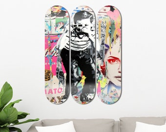 May include: Three skateboard decks with colorful, abstract art featuring a person holding a camera, a woman's face, and a pink and white background.