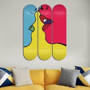 May include: Three skateboard decks with a colorful abstract design of two faces kissing. The faces are outlined in black and filled with bright colors, including yellow, blue, red, and green.