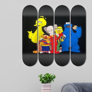 Peut inclure: Quatre planches de skate noires avec des personnages de Sesame Street imprim&eacute;s dessus. Les personnages incluent Big Bird, Elmo, Cookie Monster et un personnage de l'&eacute;mission Sesame Street portant une chemise &agrave; rayures noires et blanches.