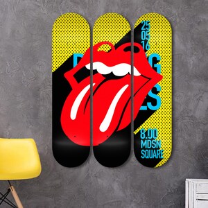 May include: Three yellow and black skateboard decks with a red tongue and lips graphic. The middle deck has the text "Rolling Stones" in blue and white. The right deck has the text "25 05 16" and "8.00 MDSN SQUARE" in blue and white.
