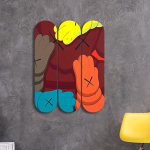 Op de afbeelding: Drie skateboard decks met een kleurrijk abstract ontwerp met een rode achtergrond, gele, oranje, blauwe en bruine vormen. Het ontwerp bevat een herhaald 'X'-patroon.