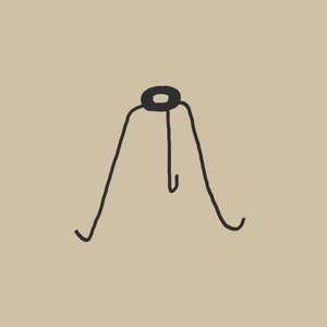 Puede incluir: Adaptador de montaje de arpa de metal negro con una altura de 5,7 cm. El adaptador tiene una parte superior circular y tres patas.