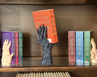 May include: A set of seven Harry Potter bookends, featuring a black and a beige hand-shaped bookend. The bookends are holding up a copy of "Harry Potter and the Deathly Hallows".