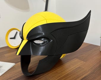 May include: A black and yellow plastic Wolverine mask with a textured surface. The mask has a detailed design with a black eye mask and a yellow stripe down the center.