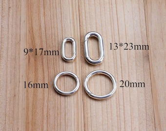 May include: Four silver-colored metal rings and loops of varying sizes are displayed on a wooden surface. The sizes are labeled as 9*17mm, 13*23mm, 16mm, and 20mm. The objects are likely jewelry findings or hardware.