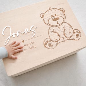Puede incluir: Una caja de madera para recuerdos con un acabado marrón claro. La caja está grabada con el nombre "Jonas", un corazón y la fecha "ember 2024". También incluye la hora "0:58 Uhr" y el peso "3300 g". Un oso de peluche de dibujos animados está grabado en la caja.