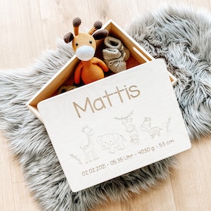Puede incluir: Una caja de recuerdos de madera con un acabado de madera clara. La tapa está abierta y presenta una inscripción personalizada con el nombre "Mattis", una fecha de nacimiento "02.02.2021", una hora de nacimiento "05:35 Uhr", un peso de "4030 g" y una longitud de "53 cm". La caja está decorada con una jirafa, un elefante y monos.
