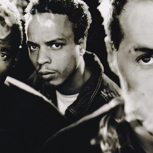 May include: Sepia-toned portrait of three men, each with a serious expression. One man is smoking, with smoke visible. The image is a close-up, focusing on the faces and upper torsos. The men appear to be of African descent and are wearing casual clothing.