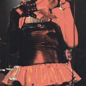 May include: A woman wearing a black and silver top with a ruffled skirt, singing into a microphone. She is wearing black gloves and a silver necklace.