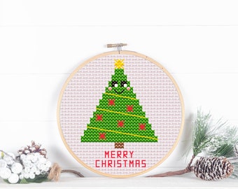 May include: A cross-stitch Christmas tree design in a wooden hoop. The green tree has red ornaments, yellow star, and sunglasses. The words "MERRY CHRISTMAS" are stitched in red below the tree. The background is a light pink fabric.