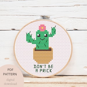 Può includere: Schema di punto croce con un simpatico cactus con un fiore rosa in cima, in un vaso marrone, con il testo "Don't be a prick" sotto. Lo schema è in un telaio da ricamo in legno.