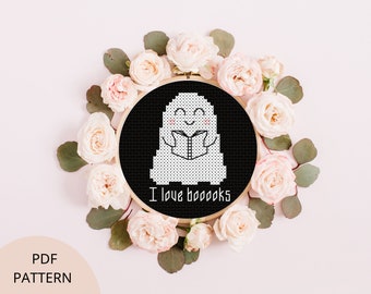 May include: A white ghost with a smiling face is reading a book. The ghost is surrounded by a wreath of pink roses. The text below the ghost reads "I love booooks".