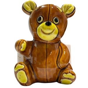 May include: A glossy ceramic bear figurine featuring a rich brown body with bright yellow accents on the ears, muzzle, paw pads, and feet. The bear has a friendly expression with dark eyes and a small black nose, depicted in a seated position.