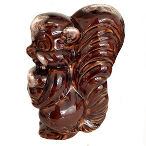 May include: A brown glazed ceramic squirrel figurine with a white glaze accent. The squirrel is holding a nut in its paws.