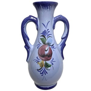 Peut inclure: Un vase en céramique bleu clair avec deux anses et un motif floral. Le vase a un motif floral bleu et blanc avec un centre rouge.