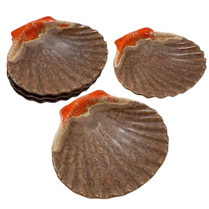 Op de afbeelding: Set van drie bruine en oranje keramische serveerschalen in de vorm van een schelp. De schalen hebben een getextureerd oppervlak en een geglazuurde oranje rand.