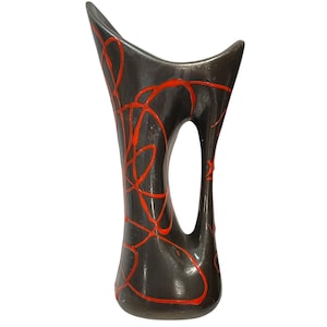 Peut inclure: Un grand vase en céramique gris foncé avec une finition lisse et brillante et une silhouette asymétrique incurvée. La surface est décorée d'un motif de lignes orange vif peint à la main qui tourbillonne sur le corps et à travers l'ouverture centrale.