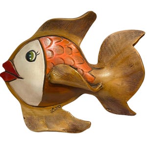 May include: A decorative fish sculpture with a whimsical design. The fish features a white face, red lips, and a green eye. The body is orange and brown, with textured details. The sculpture has a unique, artistic style.