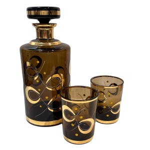 Peut inclure: Une carafe en verre brun avec un bouchon doré et un motif en spirale doré, ainsi que deux verres à boire en verre brun assortis avec des motifs en spirale dorés.