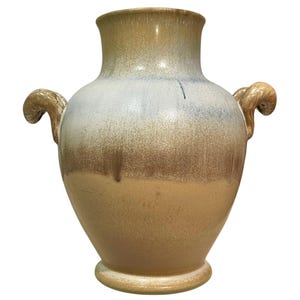 May include: A ceramic vase featuring a wide neck and a rounded body with two curved handles on the sides. The glaze transitions from a light tan at the base to a deep brown in the middle, fading into a pale blue and tan finish at the top rim.
