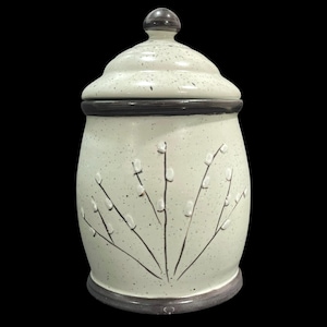 May include: A ceramic canister with a lid, featuring a speckled off-white glaze and a dark brown rim at the base and top. The body is decorated with a raised, hand-painted design of pussy willow branches in dark brown with white buds.