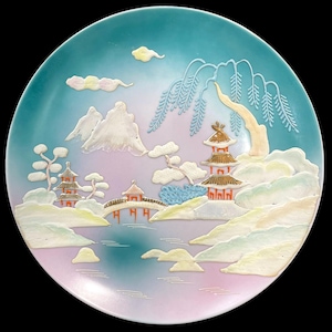 May include: A decorative plate with a Japanese landscape design. The plate features a serene scene with pagodas, mountains, and a bridge, all in a pastel color palette of blue, pink, and white. The plate has a glossy finish and a black background.