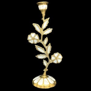 Peut inclure: Un bougeoir en laiton avec une tige en forme de plante fleurie dotée de feuilles et de deux fleurs. Les pétales, les feuilles et la base circulaire sont incrustés d'accents en nacre blanche. La coupelle supérieure accueille une bougie.