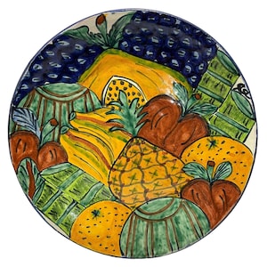 May include: A colourful ceramic plate featuring a hand-painted design of assorted fruits, including a pineapple, oranges, grapes, and apples. The plate is decorated in shades of green, yellow, orange, red, and blue.