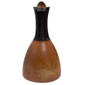 May include: A ceramic decanter featuring a wide, rounded base with a textured, speckled terracotta-colored finish. The tall, slender neck is finished in a smooth, glossy dark brown glaze, and the top includes a small, integrated pouring spout.