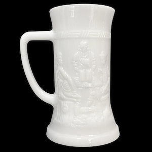 Peut inclure: Chope à bière en verre blanc laiteux avec une anse et un motif en relief détaillé. Le relief représente des personnages autour d'une table. La chope a une base large et un sommet légèrement évasé.