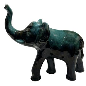 May include: A ceramic elephant figurine in shades of teal and black. The elephant has its trunk raised and is standing on four legs. The glossy finish gives the figurine a polished look. This decorative item is suitable for home decor.
